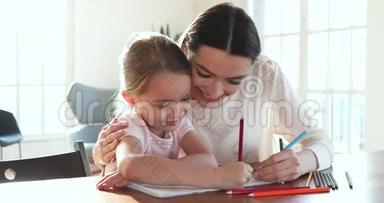 关爱的妈妈拥抱帮助的女儿用铅笔画画